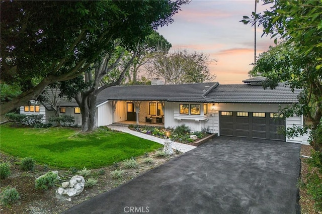 view of front of house featuring driveway, a garage, a tile roof, a chimney, and a front yard