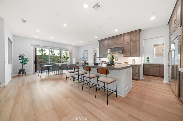 kitchen with light wood-style flooring, under cabinet range hood, a breakfast bar, visible vents, and an island with sink