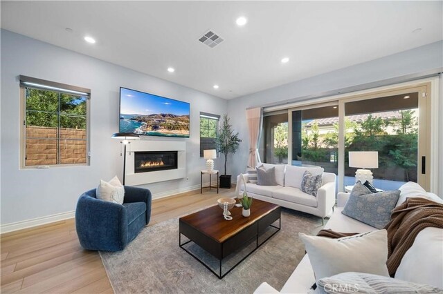 living area with a glass covered fireplace, wood finished floors, visible vents, and recessed lighting