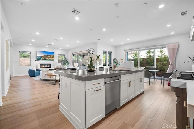 kitchen with visible vents, a glass covered fireplace, dark countertops, light wood-style flooring, and a sink