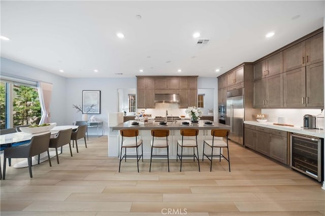 kitchen with built in fridge, visible vents, beverage cooler, under cabinet range hood, and a kitchen breakfast bar