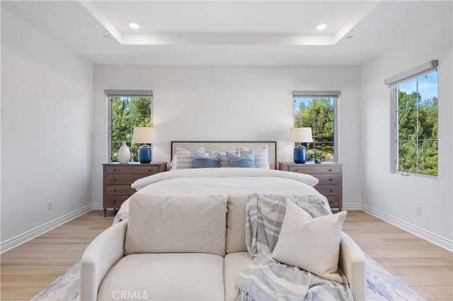 bedroom with light wood-style flooring, baseboards, a raised ceiling, and recessed lighting