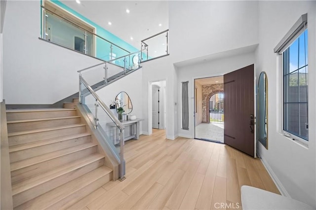 entrance foyer with stairs, a healthy amount of sunlight, a towering ceiling, and wood finished floors