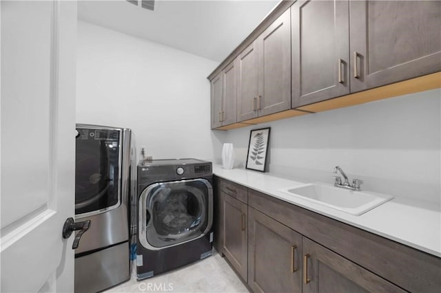 clothes washing area with washing machine and dryer, cabinet space, and a sink