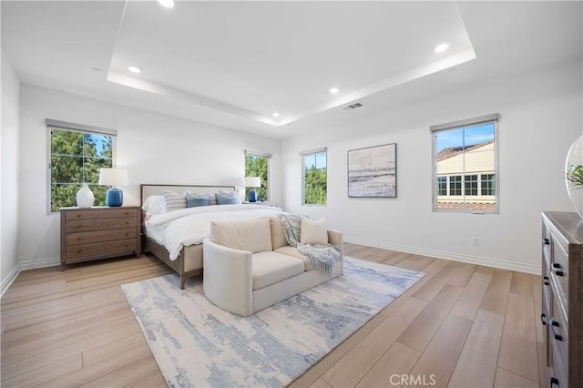 bedroom featuring light wood-style flooring, baseboards, and a raised ceiling