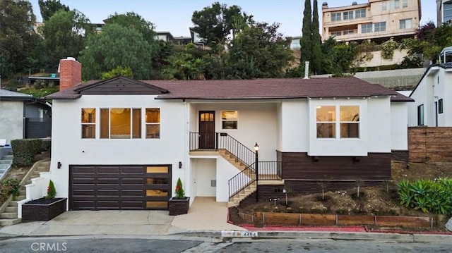 view of front of house with a chimney, stairs, concrete driveway, stucco siding, and a garage