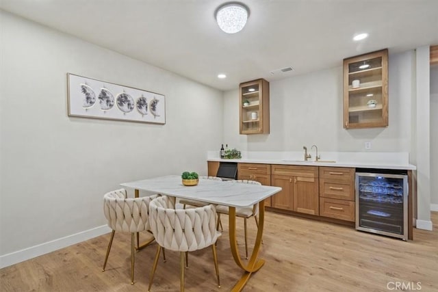 kitchen featuring brown cabinetry, beverage cooler, baseboards, glass insert cabinets, and light wood-type flooring