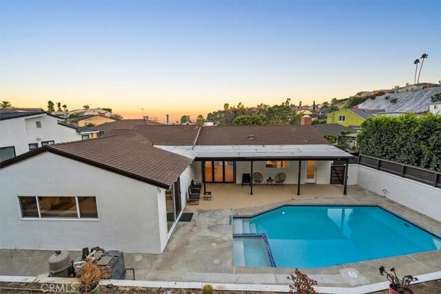 back of property at dusk with stucco siding, fence, a pool with connected hot tub, and a patio area