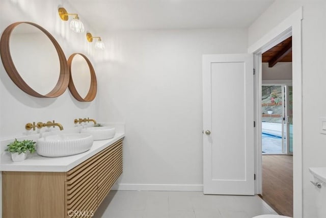 bathroom featuring double vanity, beamed ceiling, baseboards, and a sink