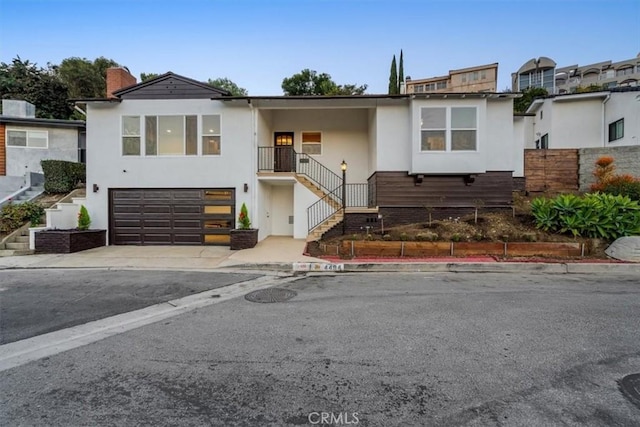 view of front of house with driveway, a chimney, stairs, stucco siding, and a garage