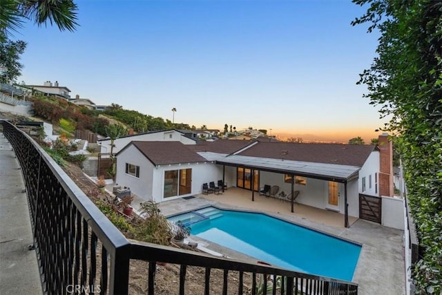 back of house at dusk featuring a patio area, a fenced backyard, and a pool with connected hot tub