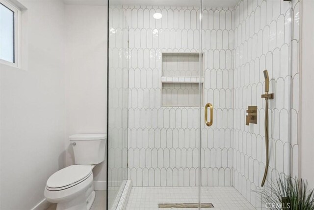 bathroom featuring toilet, tiled shower, and baseboards