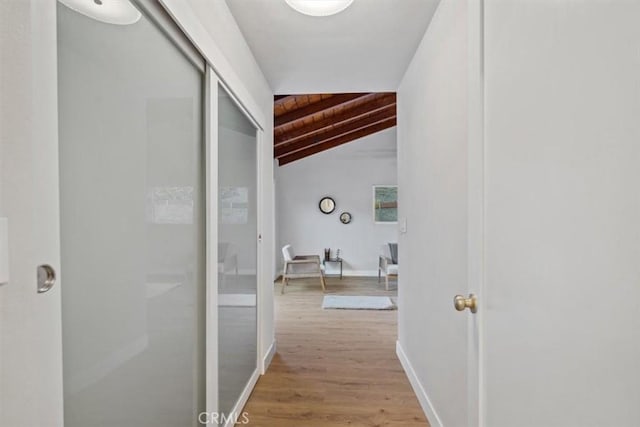 hall featuring baseboards, light wood-style floors, wood ceiling, and vaulted ceiling with beams