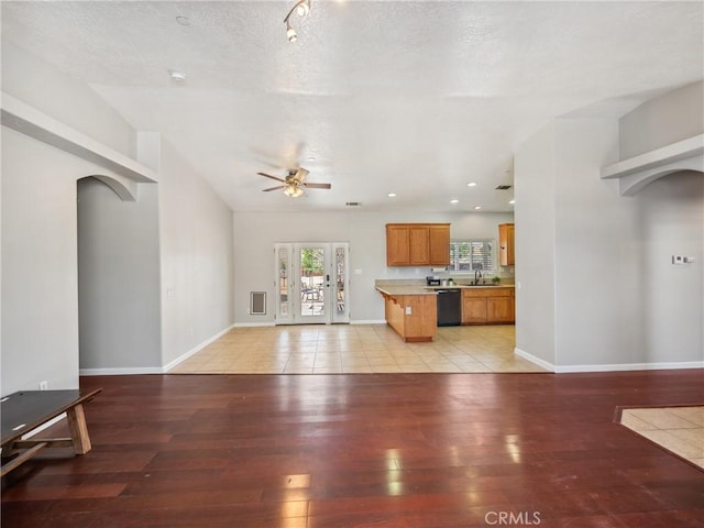 unfurnished living room featuring arched walkways, a ceiling fan, a textured ceiling, light wood-type flooring, and baseboards