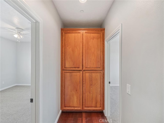 hallway with dark colored carpet and baseboards