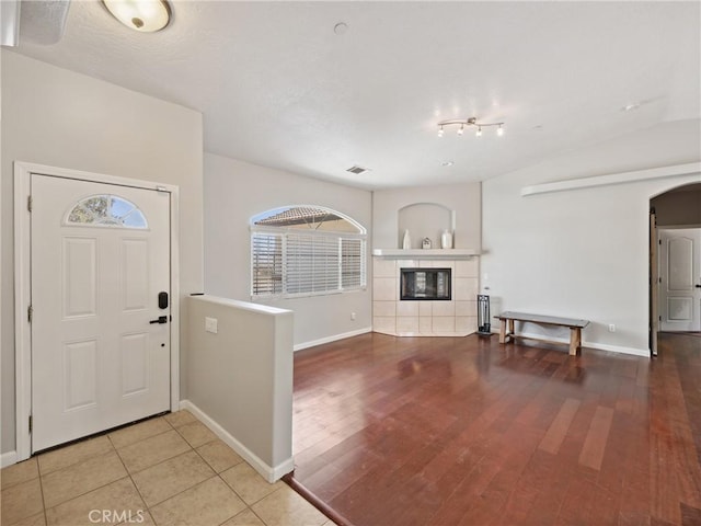 entrance foyer featuring arched walkways, visible vents, wood finished floors, a tile fireplace, and baseboards