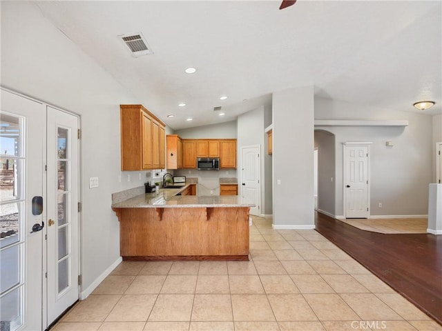 kitchen featuring light tile patterned floors, lofted ceiling, visible vents, stainless steel microwave, and a peninsula