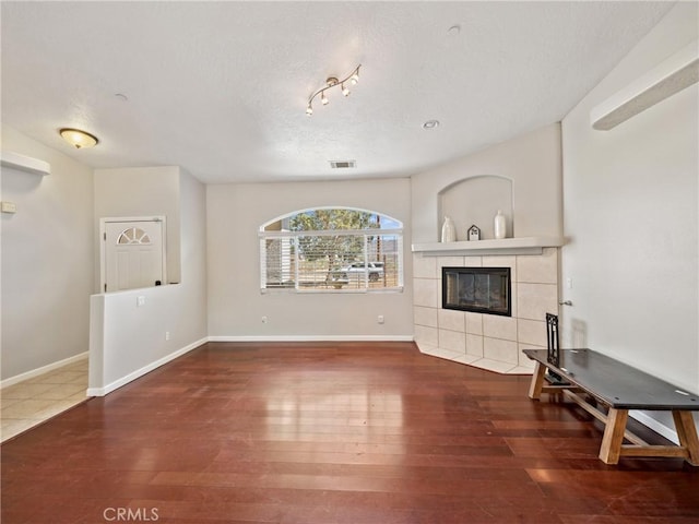 living area featuring baseboards, visible vents, a tiled fireplace, wood finished floors, and a textured ceiling