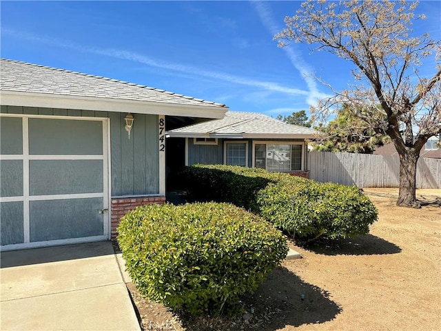 doorway to property featuring brick siding, an attached garage, and fence