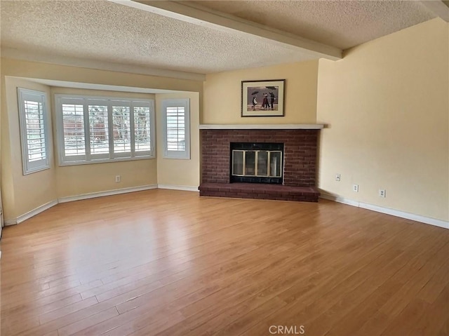 unfurnished living room featuring baseboards, wood finished floors, a textured ceiling, a brick fireplace, and beam ceiling