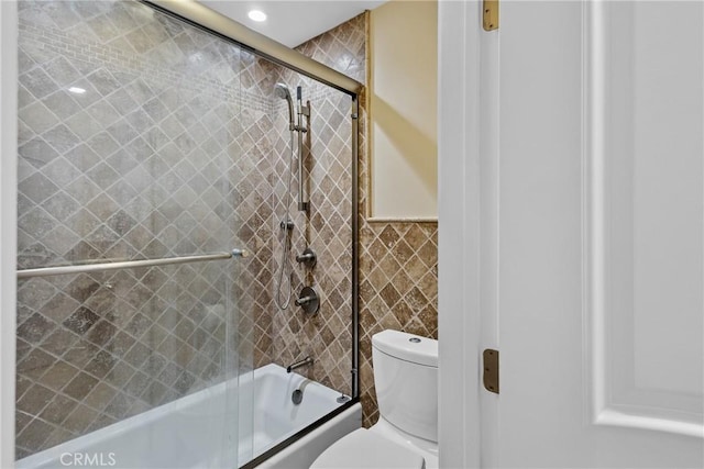 full bath with combined bath / shower with glass door, toilet, and tile walls