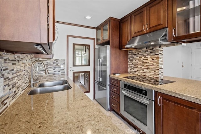 kitchen featuring glass insert cabinets, appliances with stainless steel finishes, light stone countertops, under cabinet range hood, and a sink