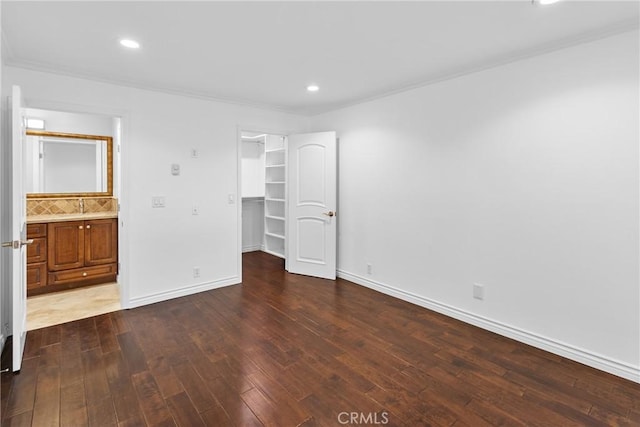 unfurnished bedroom with recessed lighting, baseboards, wood-type flooring, a walk in closet, and crown molding