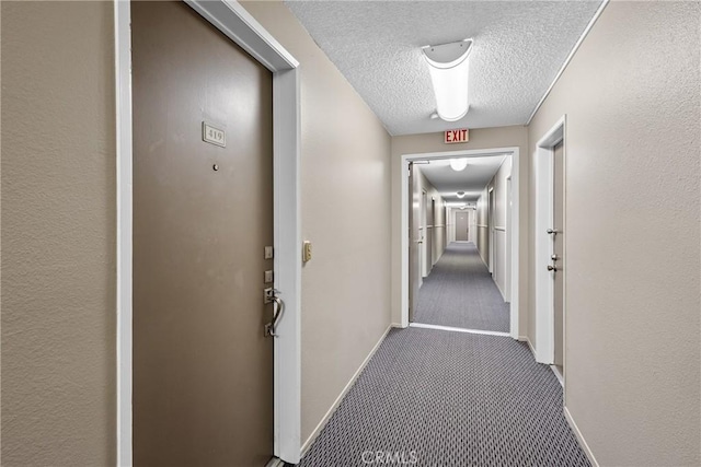 hallway with carpet, a textured wall, a textured ceiling, and baseboards