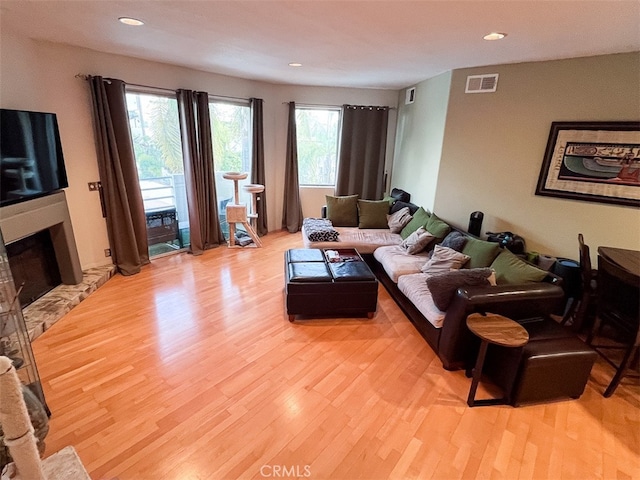 living room with a fireplace with raised hearth, light wood finished floors, visible vents, and recessed lighting