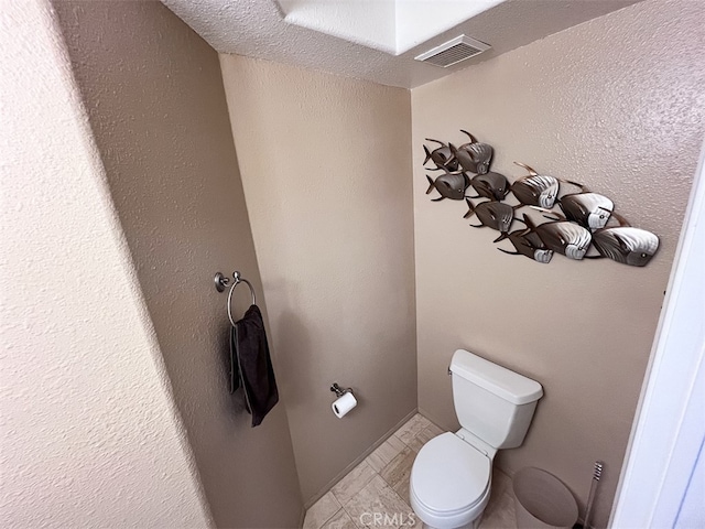 bathroom with toilet, a textured wall, and visible vents