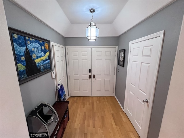 entryway with a tray ceiling, light wood-type flooring, and baseboards