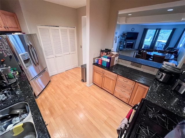 kitchen with a fireplace, light wood finished floors, brown cabinetry, black gas stove, and stainless steel fridge