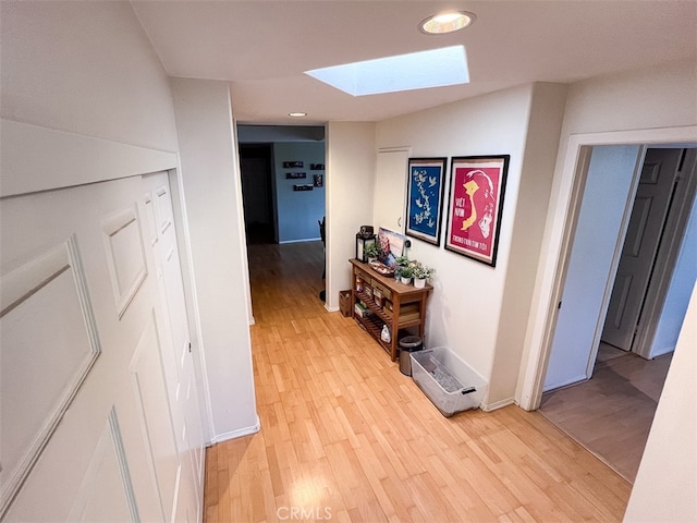 hallway with a skylight, light wood-style flooring, and baseboards