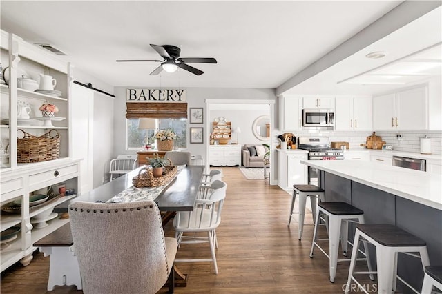 dining room with a barn door, visible vents, ceiling fan, and dark wood-type flooring