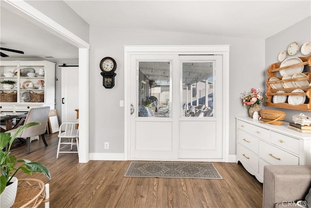 foyer entrance with ceiling fan, a barn door, dark wood finished floors, and baseboards