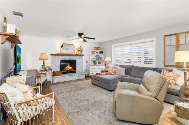 living area with a fireplace, wood finished floors, visible vents, and a ceiling fan