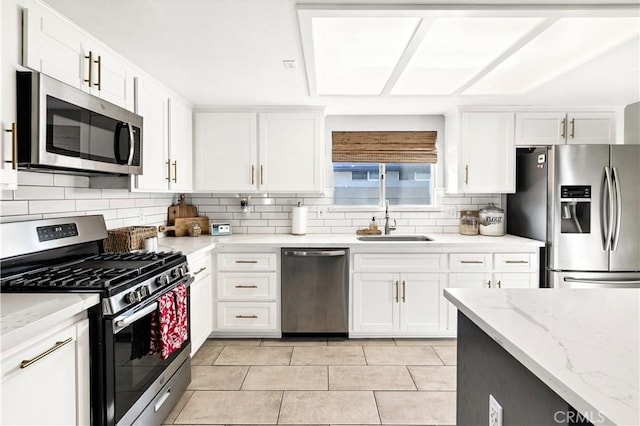 kitchen featuring light stone counters, stainless steel appliances, a sink, white cabinetry, and tasteful backsplash