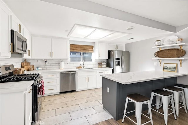 kitchen with stainless steel appliances, white cabinets, a sink, a peninsula, and a kitchen breakfast bar