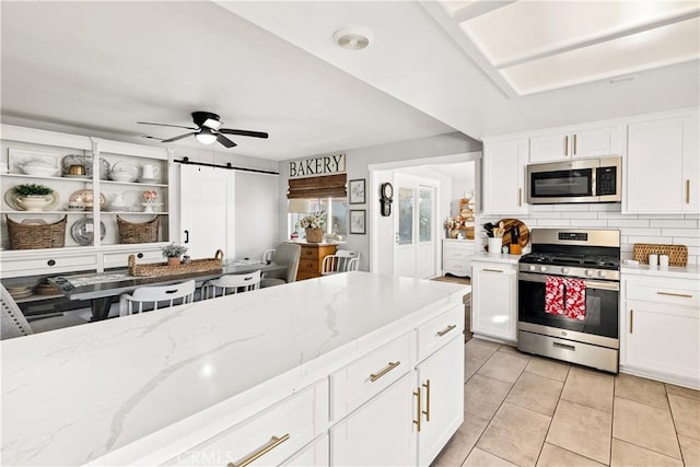 kitchen featuring light tile patterned floors, a barn door, a ceiling fan, appliances with stainless steel finishes, and tasteful backsplash