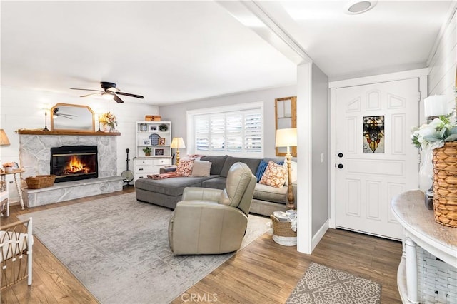 living room with ceiling fan, wood finished floors, and a stone fireplace