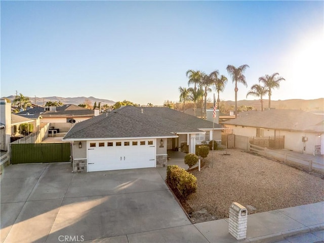 single story home featuring a garage, concrete driveway, fence, and stone siding