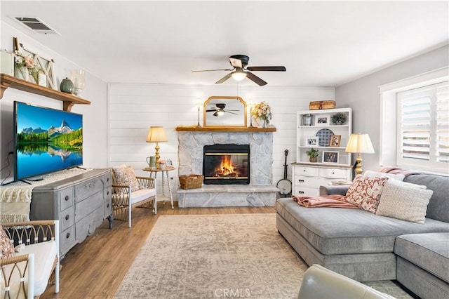 living room featuring a ceiling fan, a fireplace, visible vents, and wood finished floors