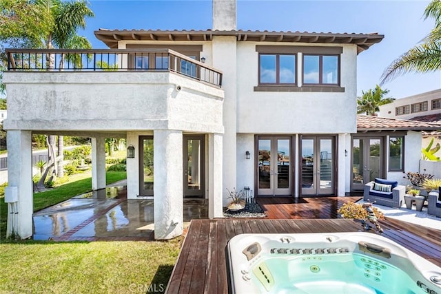 back of house featuring french doors, stucco siding, hot tub deck surround, a balcony, and a wooden deck