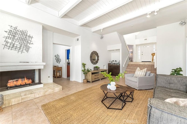 living area featuring tile patterned flooring, stairs, a lit fireplace, beamed ceiling, and track lighting