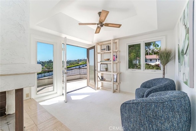 living area featuring carpet, ceiling fan, and a tray ceiling