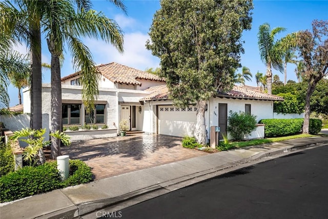 mediterranean / spanish-style house featuring a garage, decorative driveway, a tile roof, and stucco siding