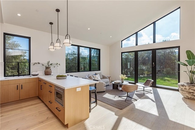 kitchen with decorative light fixtures, light countertops, stainless steel microwave, light brown cabinetry, and a peninsula