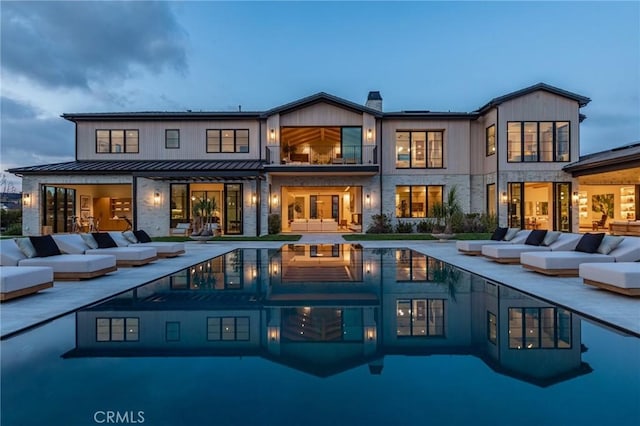 rear view of property with an outdoor pool, a standing seam roof, outdoor lounge area, and a patio