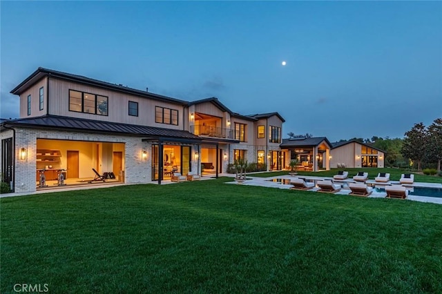 back of property featuring a patio area, a standing seam roof, brick siding, and a yard