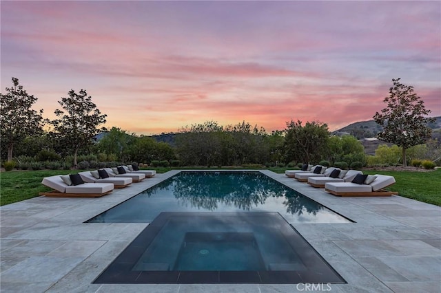 pool at dusk with an outdoor pool, a patio, and an in ground hot tub